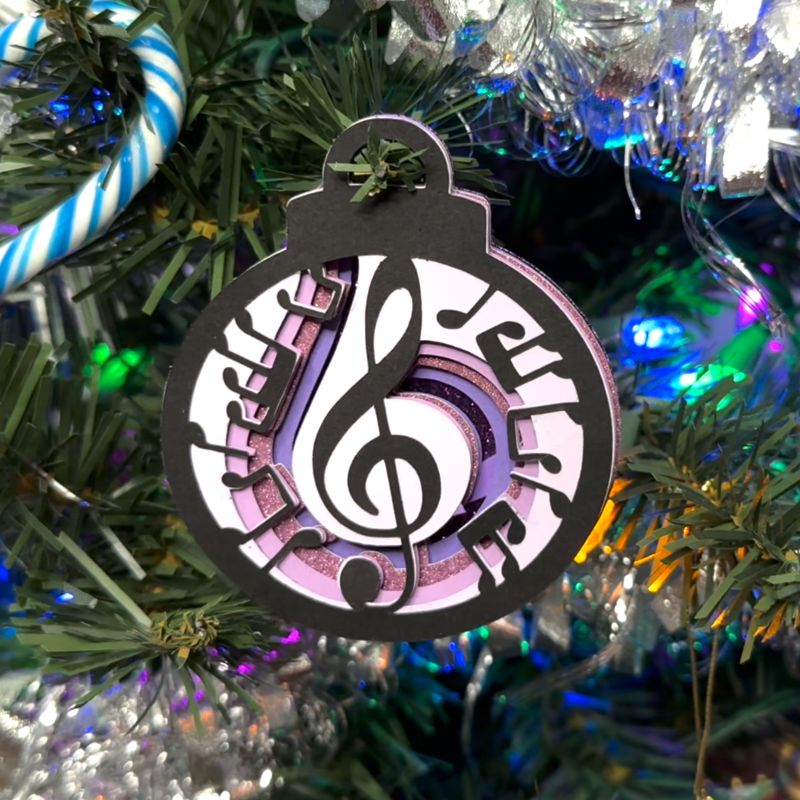 Handmade layered paper Music Notes Ornament hanging on a Christmas tree, featuring a treble clef and swirling musical notes. Perfect DIY holiday decor.