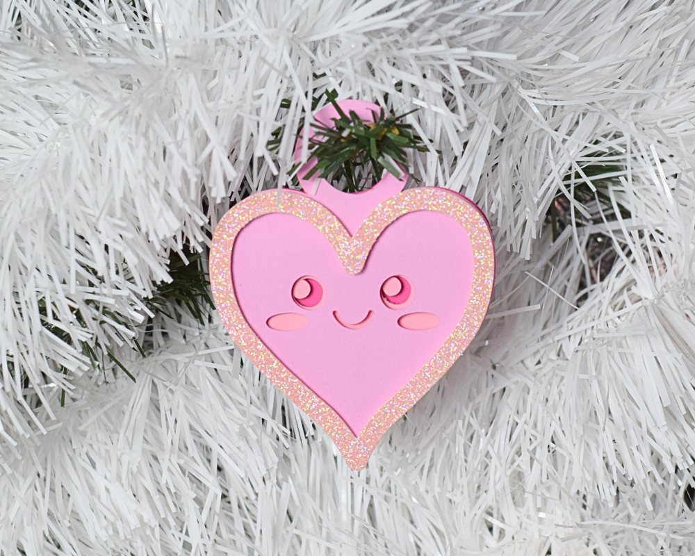 a pink heart ornament hanging from a white christmas tree