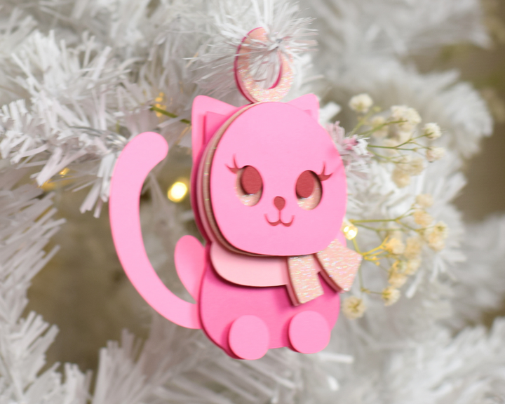 a pink cat ornament hanging from a white christmas tree