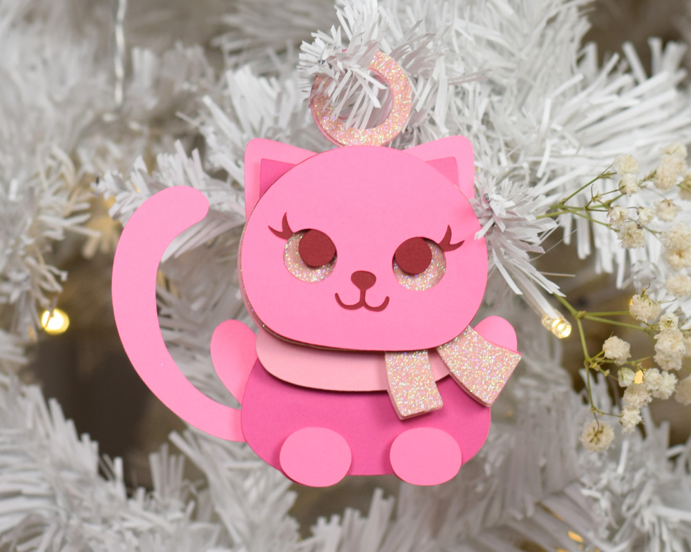 a pink cat ornament hanging from a christmas tree