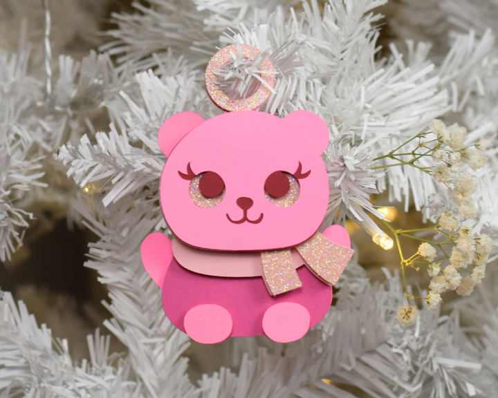 a pink bear ornament hanging from a christmas tree