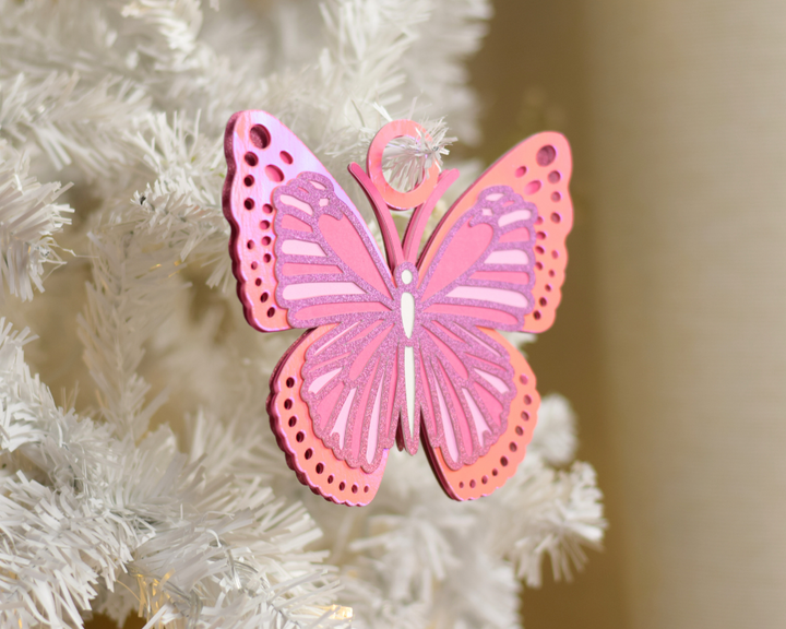 a pink butterfly ornament hanging from a white christmas tree