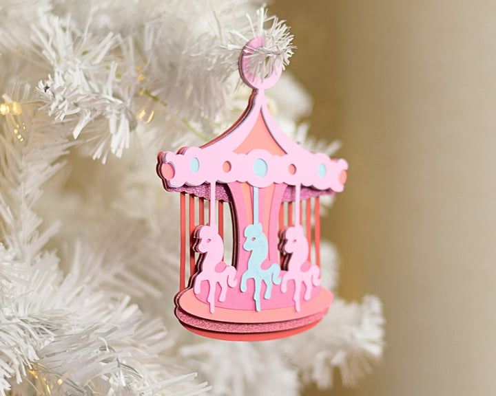 a pink carousel ornament hanging from a white christmas tree