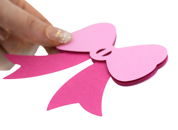 a hand holding a pink paper cut out of a bow