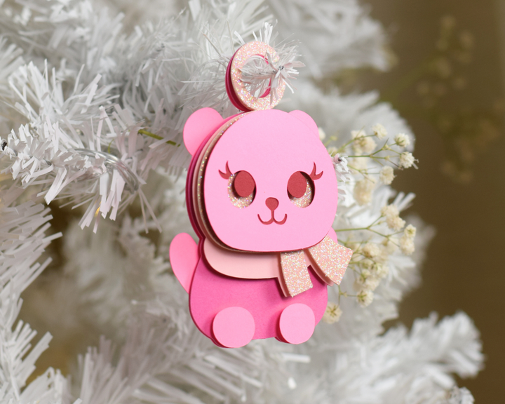 a pink bear ornament hanging from a white christmas tree