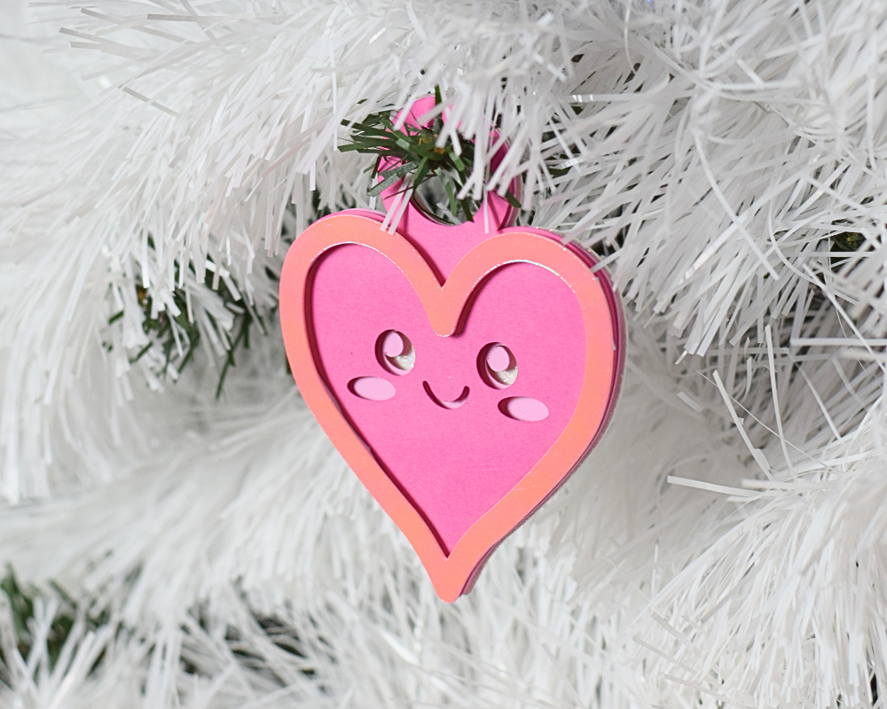 a pink heart ornament hanging from a white christmas tree